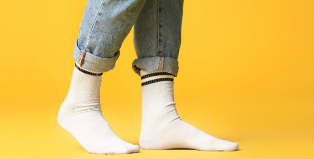 Close-up of white socks worn with rolled-up jeans on a yellow background.